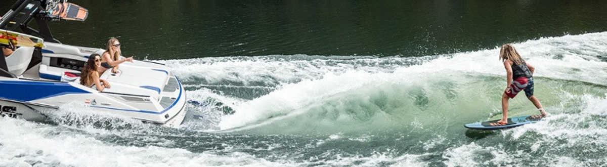Wakeboarder riding the waves behind an Axis wake boat with people watching him